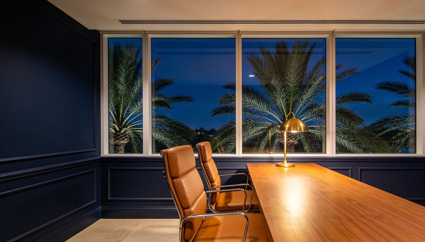 A quiet accounting office in Boca Raton at blue hour, with a walnut table, a brass lamp and palms outside